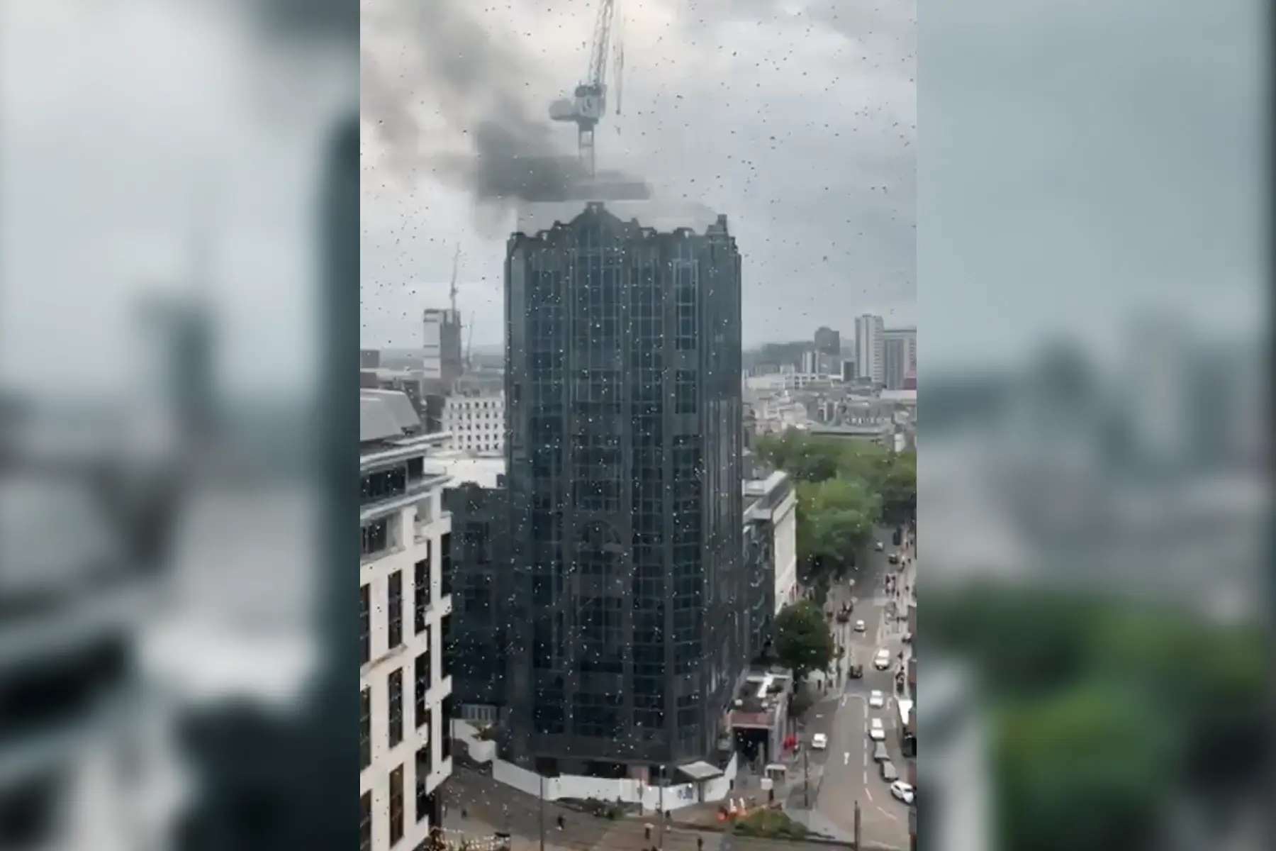 Distant view of a high-rise building with smoke rising from the roof, a clear visual of Renovation Fire Risks.