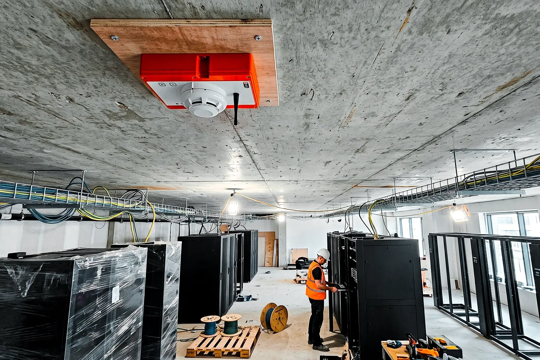 Ramtech WES wireless smoke detector fixed to a concrete ceiling above server racks being installed in a data centre