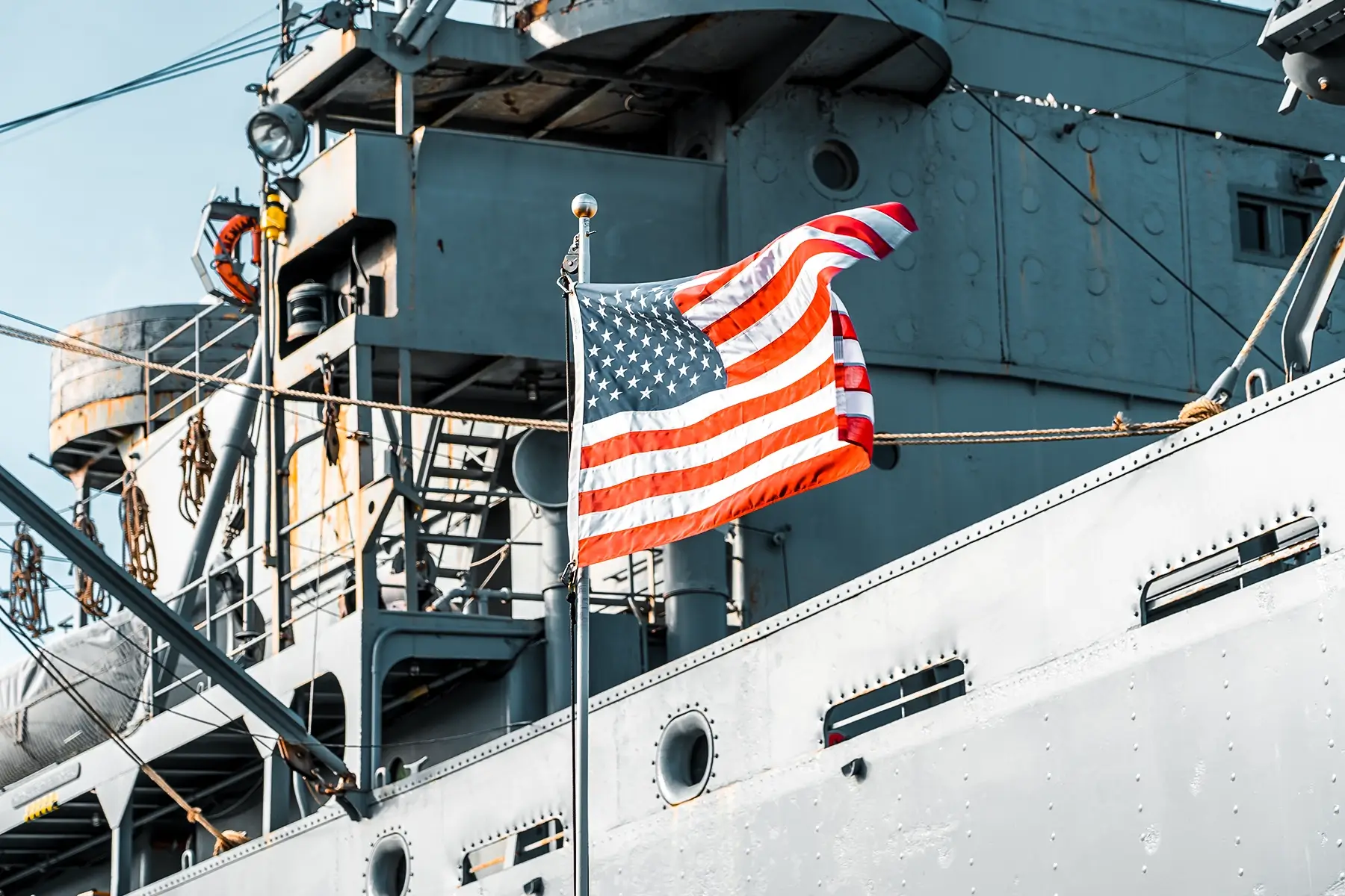A United States flag flying prominently against the grey hull of a ship in a dry dock, illustrating a location where a WES wireless life safety system is vital.