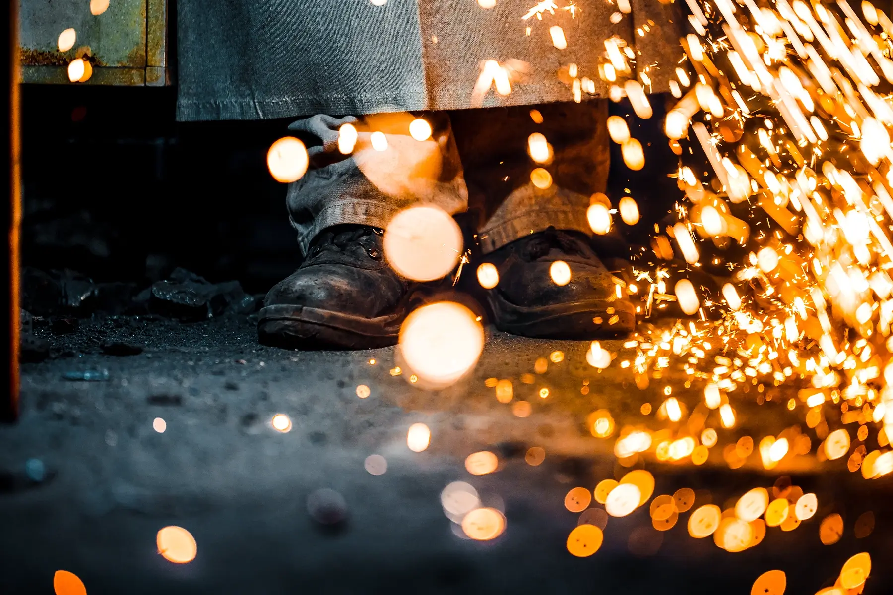 Close-up of welding sparks illuminating the floor and the boots of a worker, illustrating the hazards that require a WES wireless life safety system.