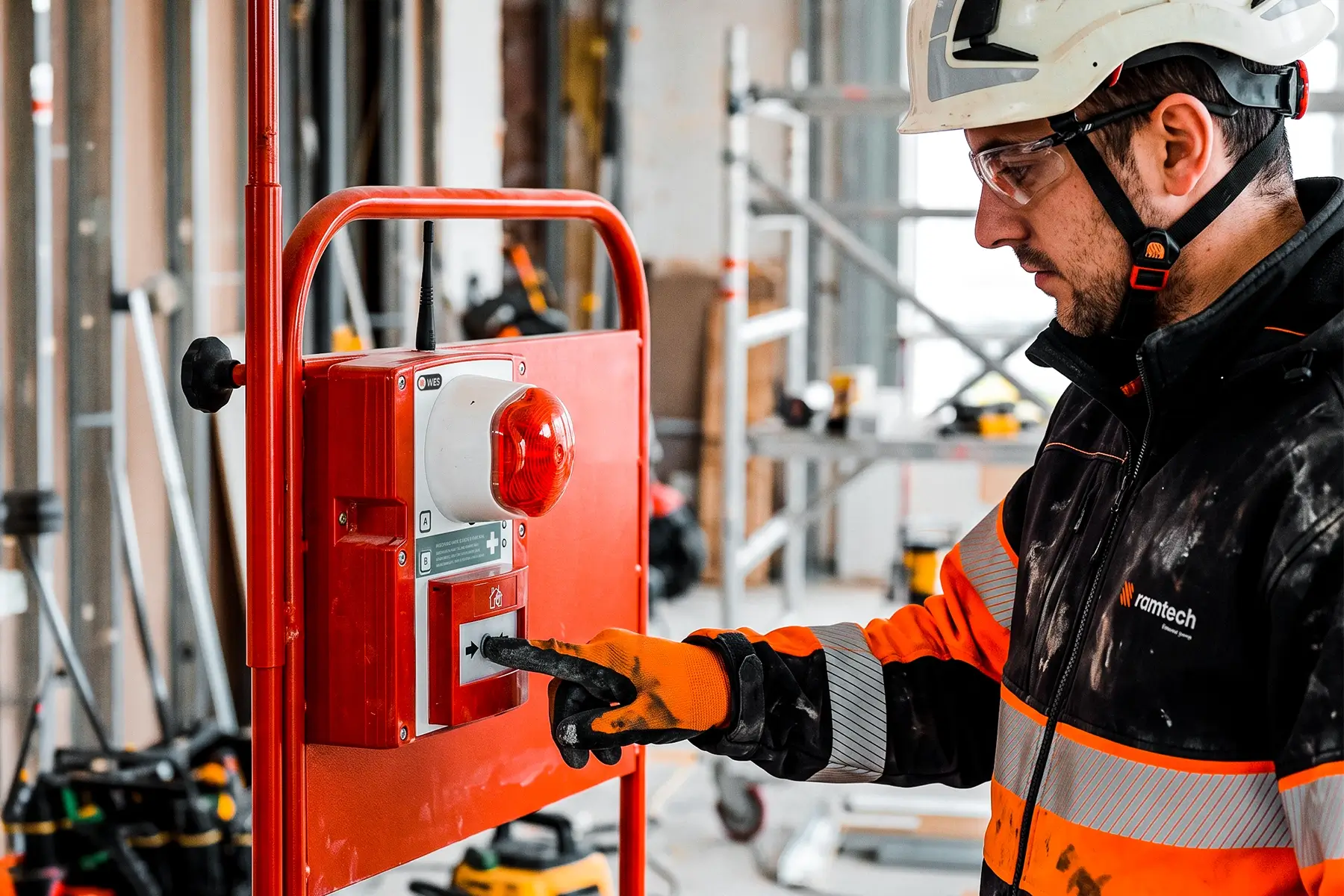 Ramtech worker in hard hat and hi-vis pressing a WES wireless fire alarm call point with red beacon on site